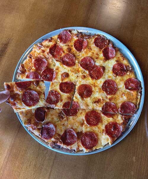 Taking a slice of thin crust pepperoni pizza